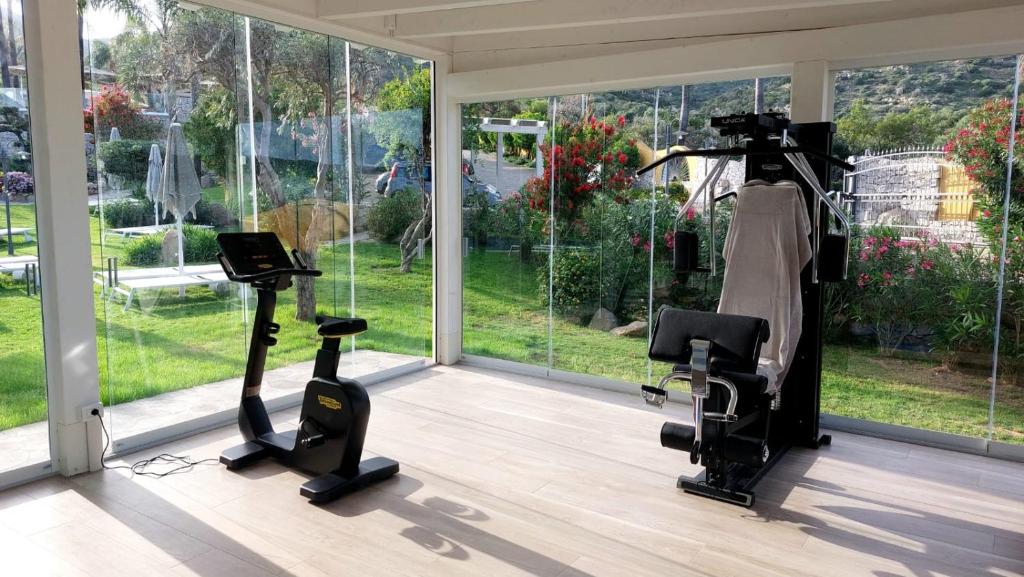 - une salle de sport avec 2 tapis de course et des vélos elliptiques dans une pièce dotée de fenêtres dans l'établissement Cruccùris Resort - Adults Only, à Villasimius