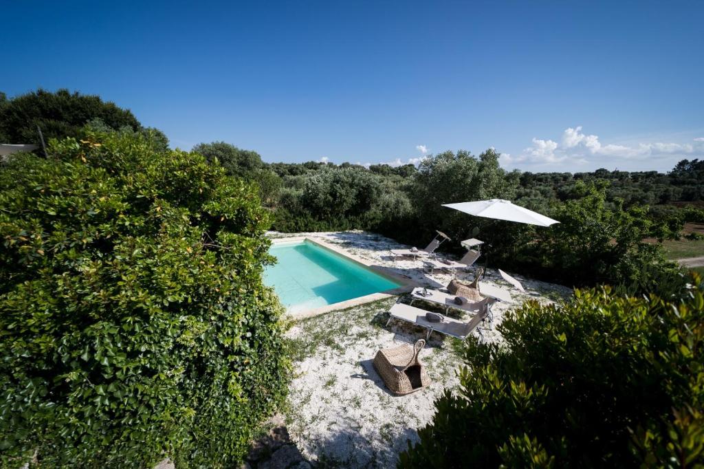 - une vue sur la piscine avec des chaises et un parasol dans l'établissement Trullo Melchiorre, à Ostuni