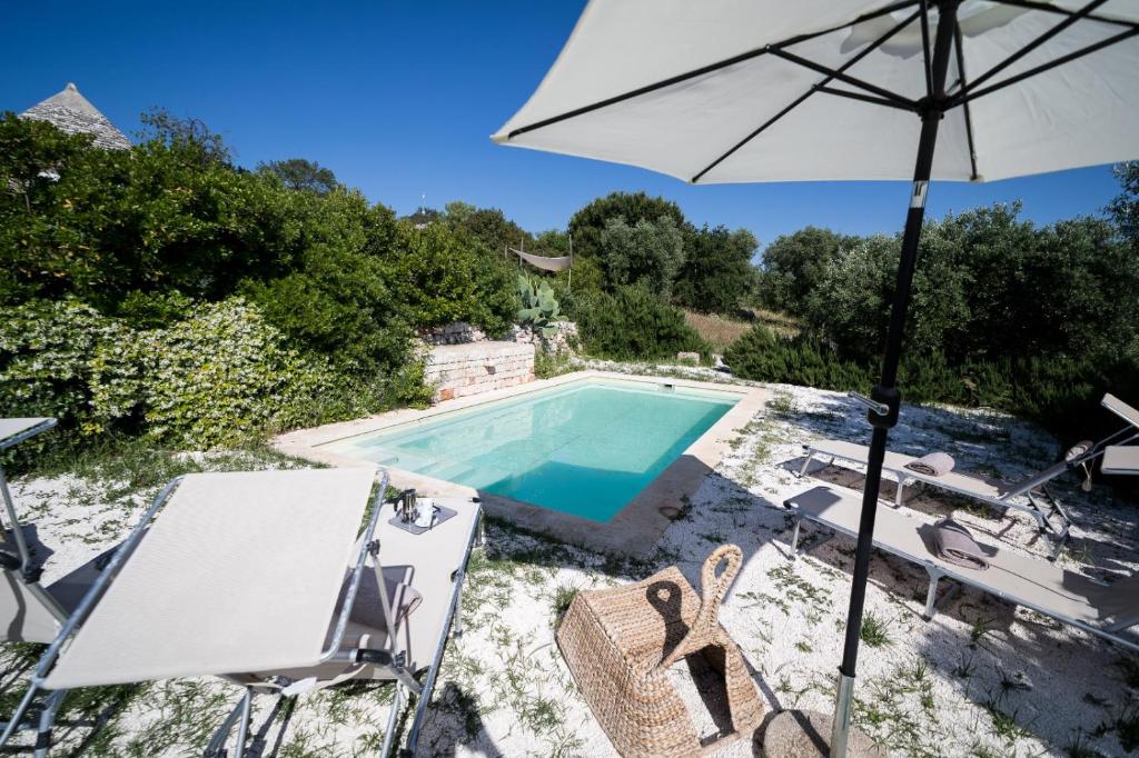 une piscine avec un parasol et des chaises et une table et un parasol dans l'établissement Trullo Melchiorre, à Ostuni
