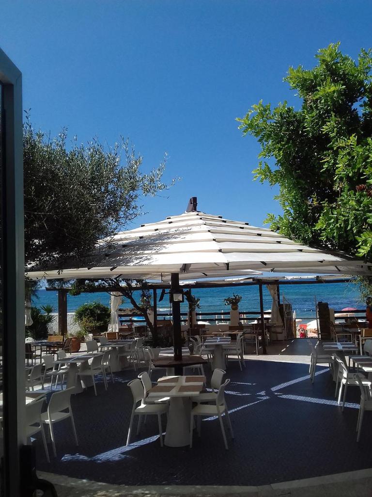 un groupe de tables et de chaises sous un parapluie dans l'établissement Hotel e Residence Il Faro Acciaroli, à Acciaroli