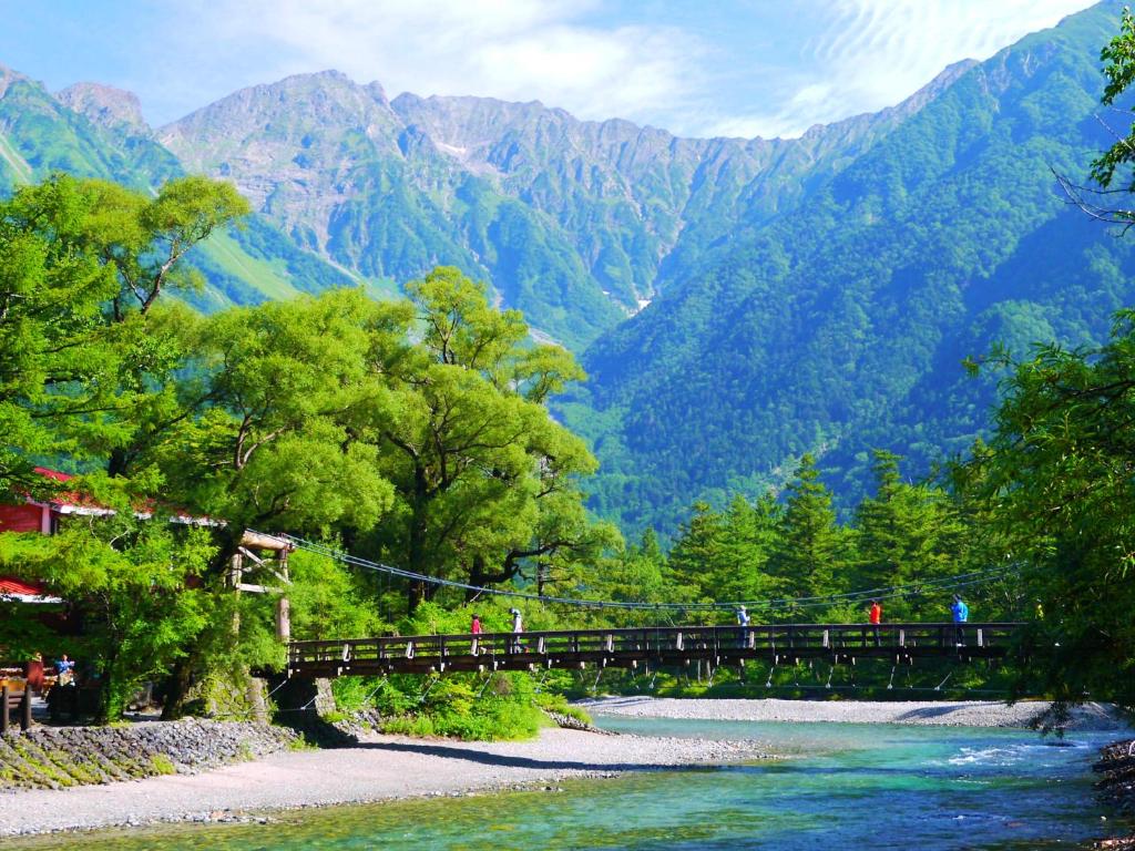 un pont sur une rivière avec des montagnes en arrière-plan dans l'établissement 雀の宿 やぐら, à Matsumoto