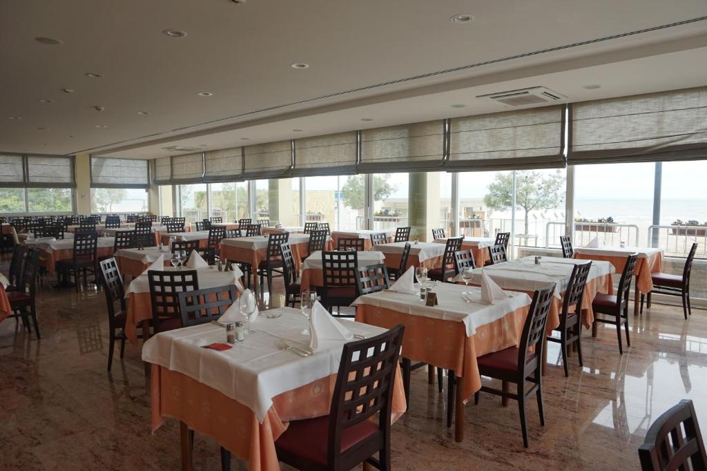 une salle à manger avec tables, chaises et fenêtres dans l'établissement Hotel Columbus, à Lignano Sabbiadoro