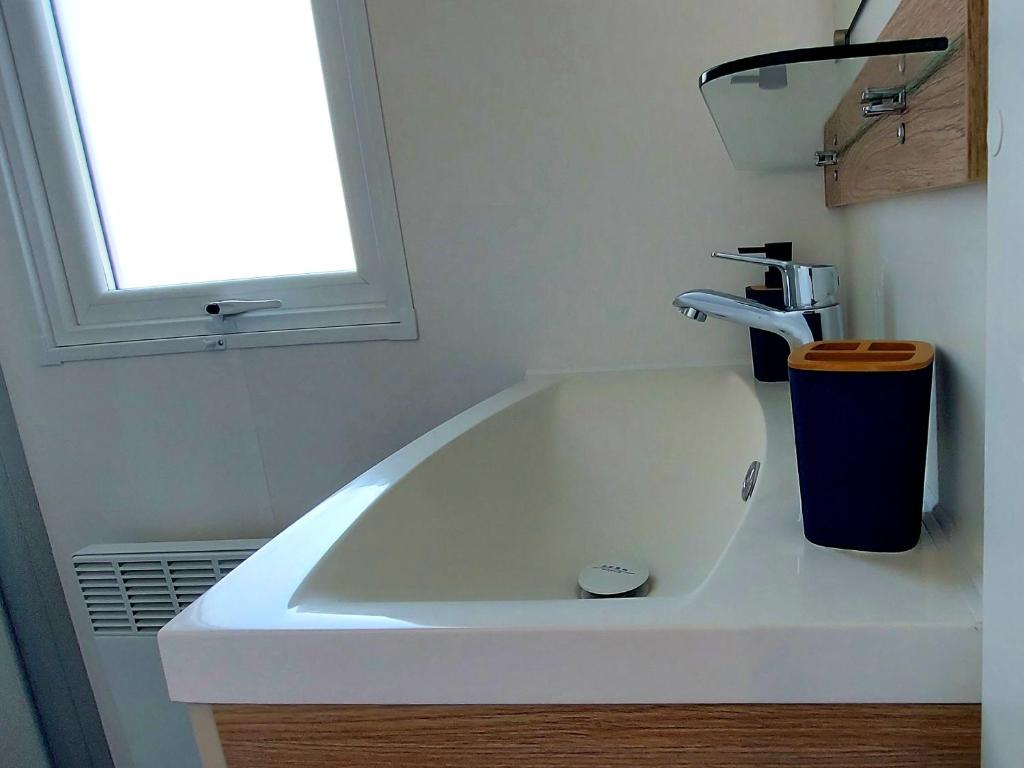 La salle de bains est pourvue d'un lavabo blanc et d'une fenêtre. dans l'établissement Mobil Home Camping Les VIVIERS, Claouey, à Claouey