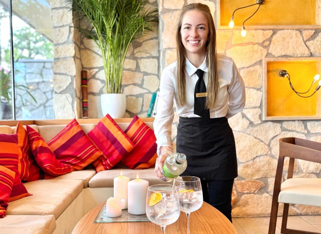 une femme debout à côté d'une table avec des verres à vin dans l'établissement Hotel Du Lac - Relax Attitude Hotel, à Brenzone