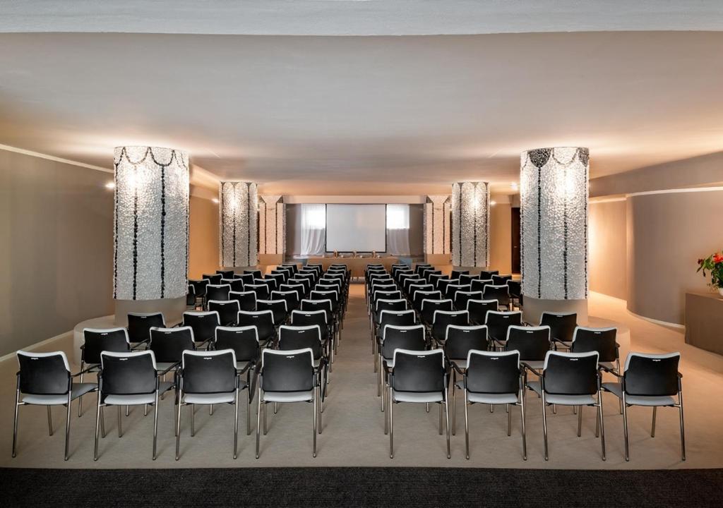 une salle de conférence avec des chaises et un écran de projection dans l'établissement Tombolo Talasso Resort, à Marina di Castagneto Carducci 60 autres photos