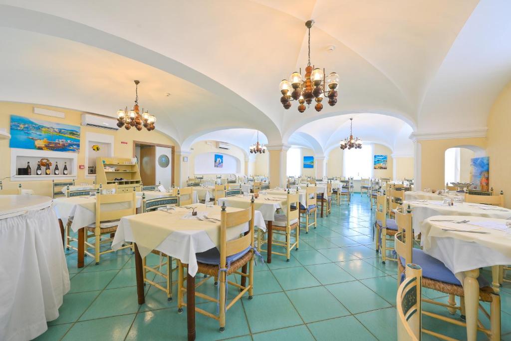 un restaurant avec des tables et des chaises blanches et des lustres dans l'établissement Av Club Terme Colella, à Ischia