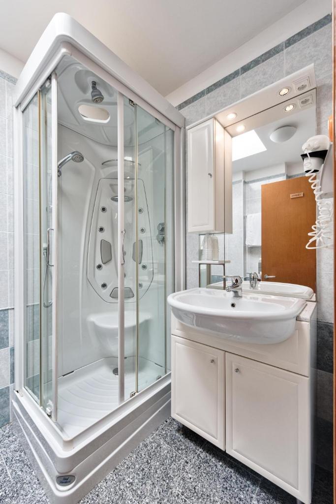 une salle de bain blanche avec une douche et un lavabo dans l'établissement Hotel Flora, à Lignano Sabbiadoro