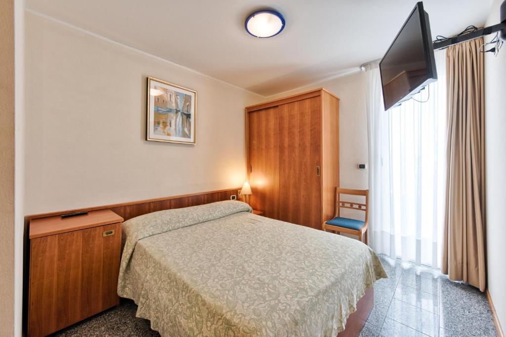 une chambre avec un lit et une télévision à écran plat dans l'établissement Hotel Flora, à Lignano Sabbiadoro