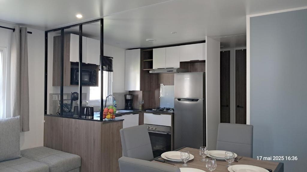 une cuisine avec une table et un réfrigérateur en acier inoxydable dans l'établissement Réveillez la Belle au Bois Dormant - Bungalow moderne, confort & linge inclus, à Saint-Jean-de-Monts