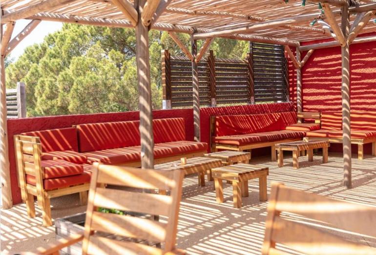 un patio avec des canapés rouges et des tables et bancs en bois dans l'établissement Mobil home climatisé 6pers. 3CH camping domaine de chaussy 5* Ardèche, à Lagorce