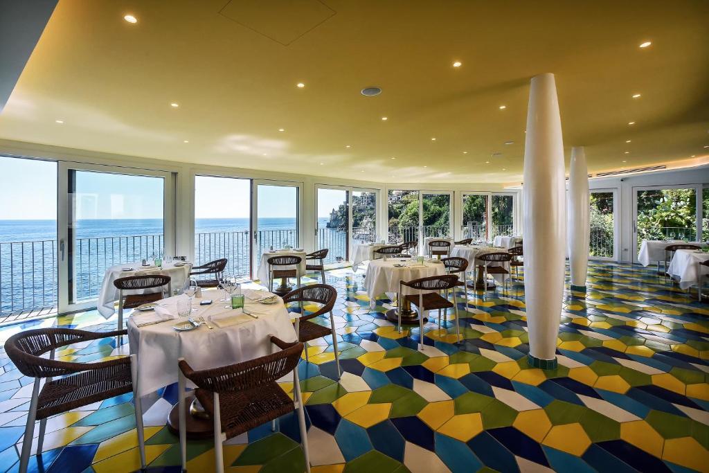 un restaurant avec des tables et des chaises dans une salle avec des fenêtres dans l'établissement Ravello Art Hotel Marmorata, à Ravello