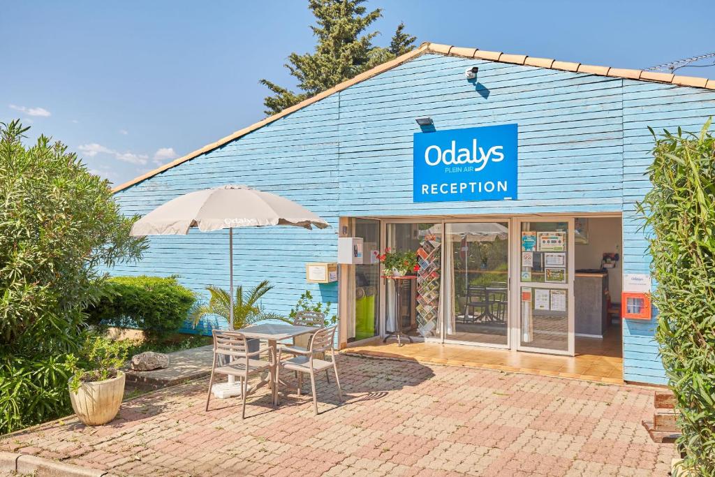 un bâtiment bleu avec une table, des chaises et un parasol dans l'établissement Domaine Résidentiel de Plein Air Odalys La Pinède, à Agde