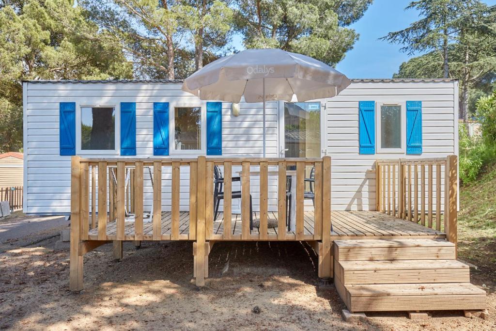 une petite maison avec un parasol et une terrasse en bois dans l'établissement Domaine Résidentiel de Plein Air Odalys La Pinède, à Agde