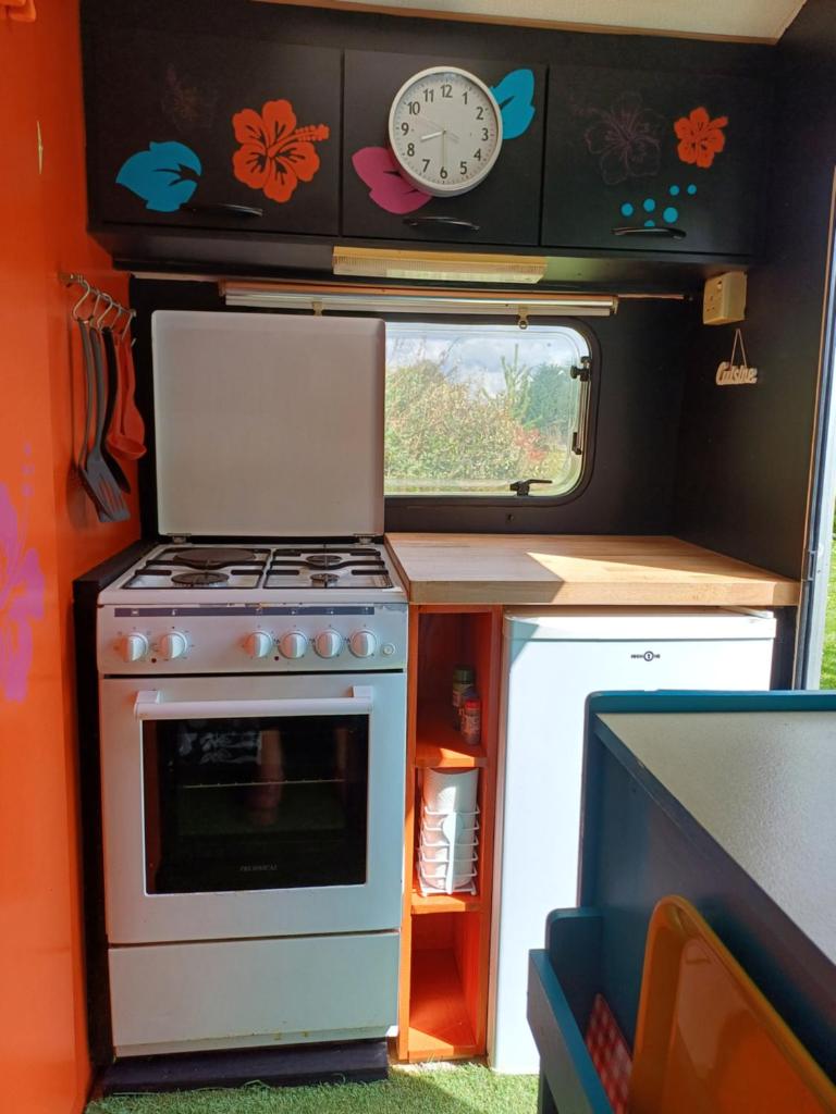 une cuisine avec une cuisinière et une horloge au mur dans l'établissement Pays de Joie - Caravan La Bohème, à Saint-Macoux