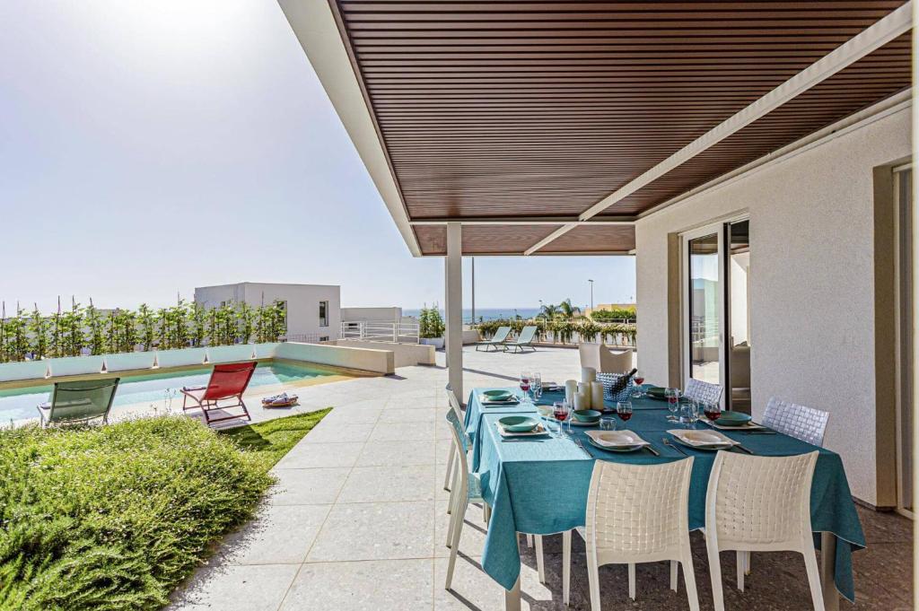 un patio avec une table et des chaises et une piscine dans l'établissement Villa Brezza Marina by Villa Plus, à Marina di Ragusa