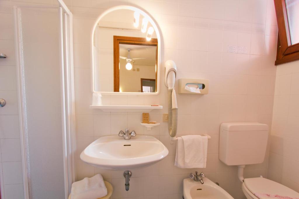 une salle de bain avec un lavabo, des toilettes et un miroir dans l'établissement Hotel Desiree, à Lignano Sabbiadoro