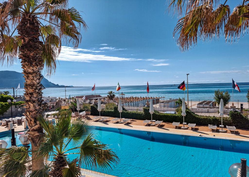 une piscine avec un palmier et l'océan dans l'établissement Hotel Sirenetta, à Isola delle Femmine