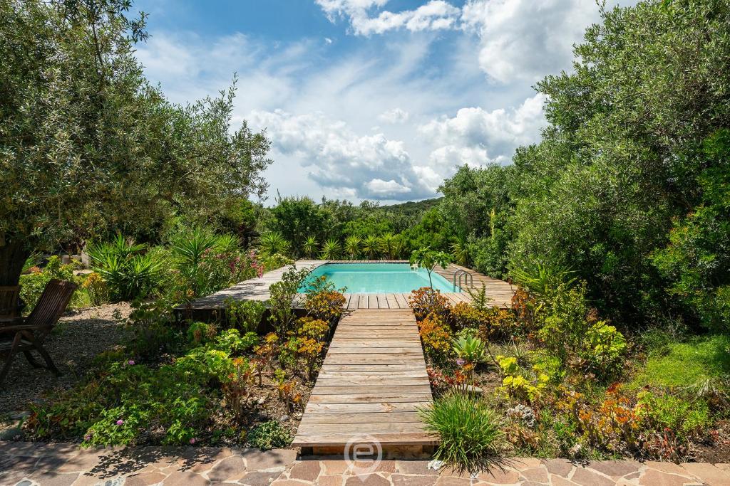 un chemin en bois menant à une piscine dans un jardin dans l'établissement Villa Barbagallo, à Porto Columbu - Perdʼe Sali