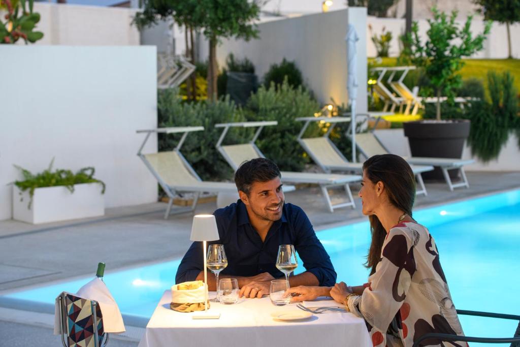 un homme et une femme assis à une table au bord d'une piscine dans l'établissement Seawater Hotel Bio & Beauty Spa, à Marsala
