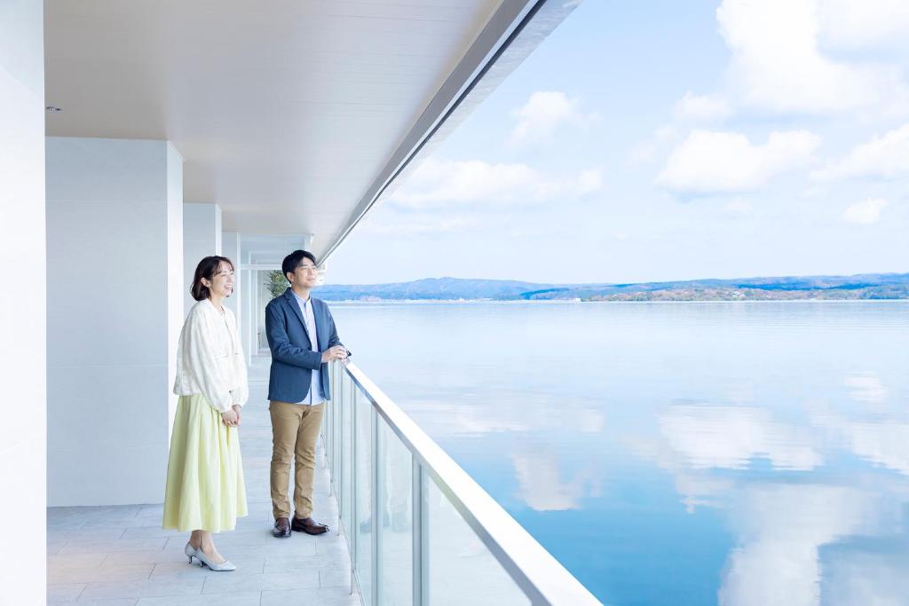 un homme et une femme debout sur un balcon regardant l'eau dans l'établissement TAOYA Wakura, à Nanao