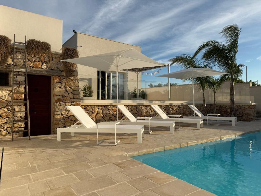 - un groupe de chaises et de parasols blancs à côté de la piscine dans l'établissement Abate Filippo apartment, à Nardò
