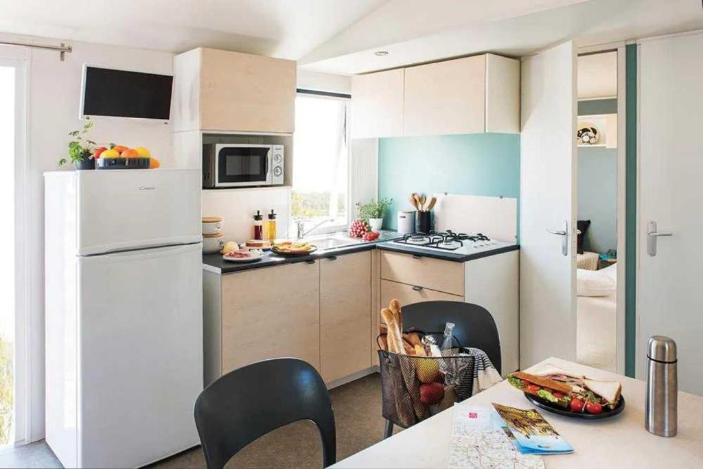 Il comprend une cuisine équipée d'un réfrigérateur blanc et d'une table avec des chaises. dans l'établissement Camping 3 étoiles - Parc aquatique - eeibbf, à Fouesnant