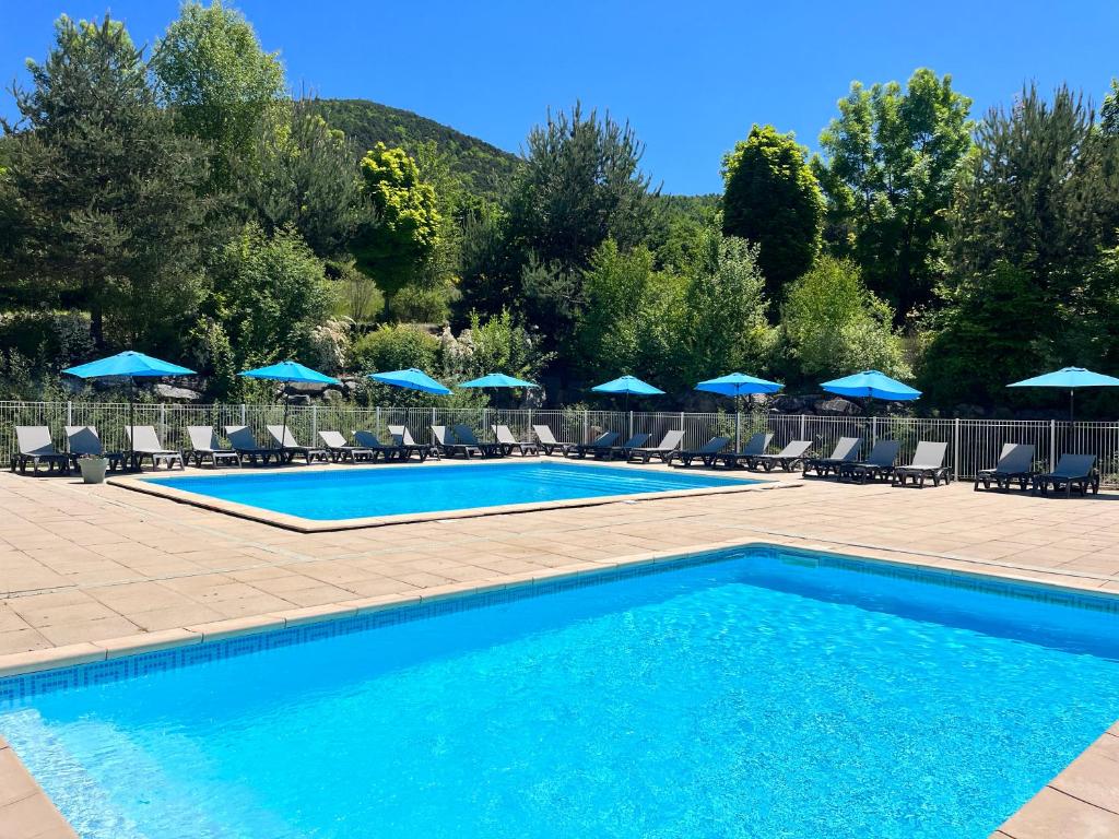 - une piscine avec des chaises et des parasols bleus dans l'établissement Village de chalets et camping La Pierre de l'Aigle, à La Bréole