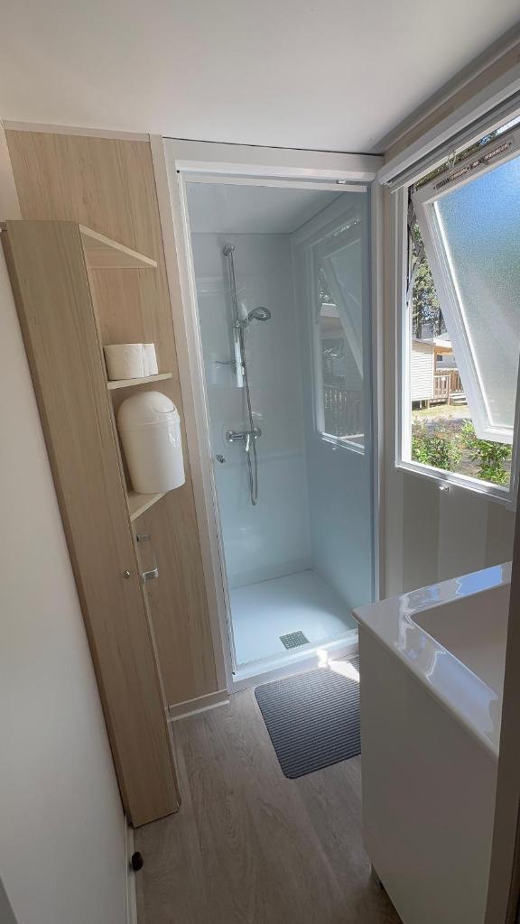 La salle de bains est pourvue d'une douche, d'un lavabo et d'une porte. dans l'établissement Mobil-home Le Manosely confort 6 pers Climatisé, à Agde