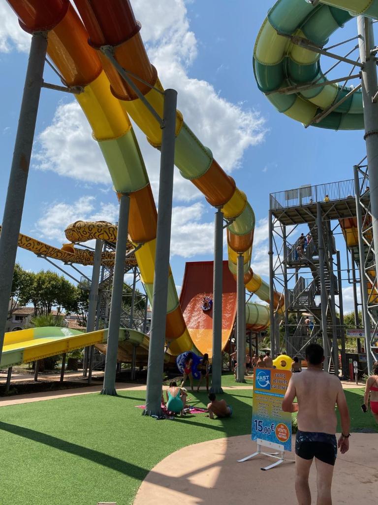 un homme marchant devant des montagnes russes dans un parc dans l'établissement Mobil-home Le Manosely confort 6 pers Climatisé, à Agde