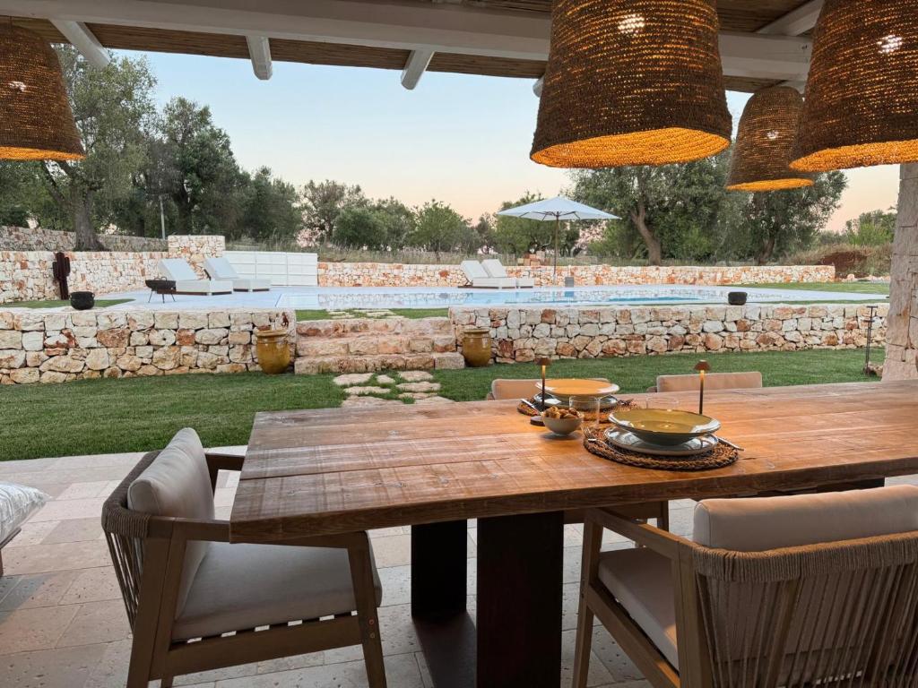 une table et des chaises en bois dans un patio avec un mur en pierre dans l'établissement Trullo di Theo, à Ostuni