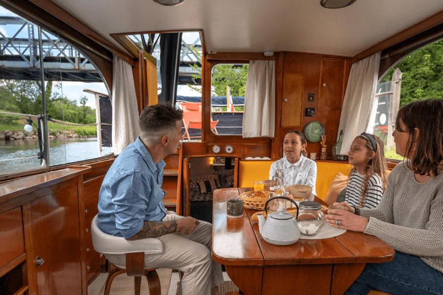 Un groupe de personnes assises à une table dans un bateau dans l'établissement SEALOV Hébergements insolites- linge, ménage et vélos inclus, à Eaucourt-sur-Somme