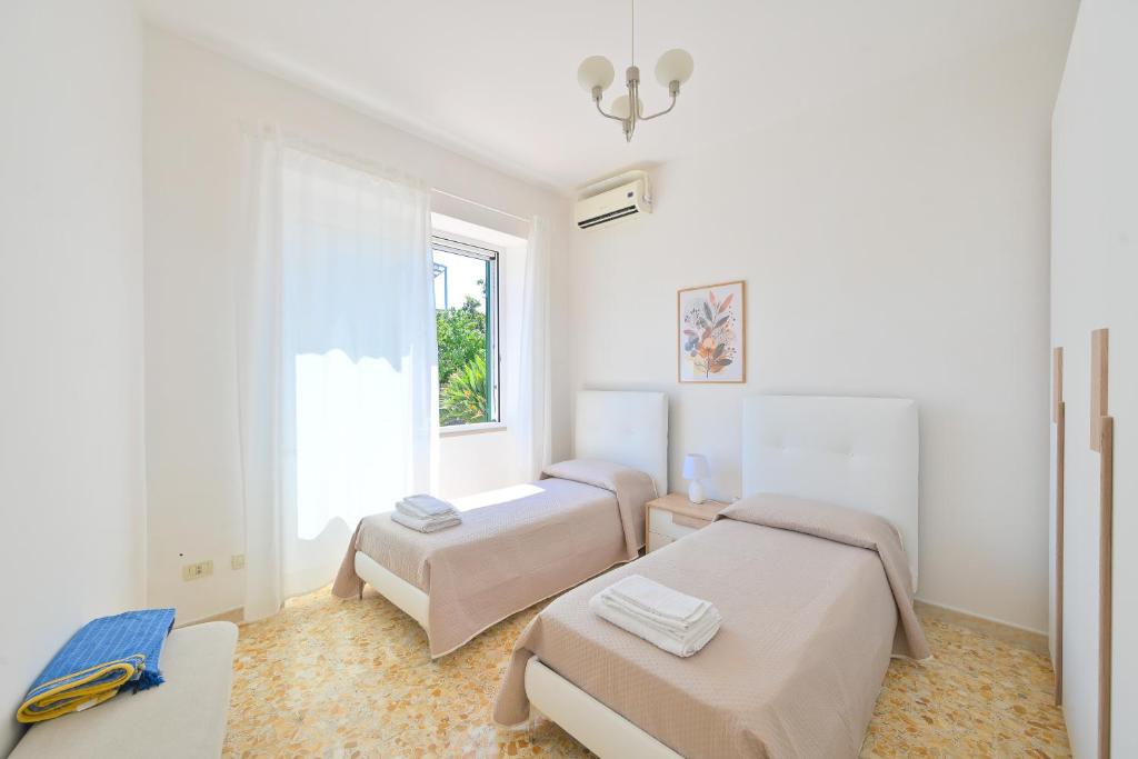 Cette chambre blanche dispose de deux lits et d'une fenêtre. dans l'établissement Villa Maddalena Ischia Giardino Privato e Parcheggio - Perfetta per 6 Ospiti, à Ischia