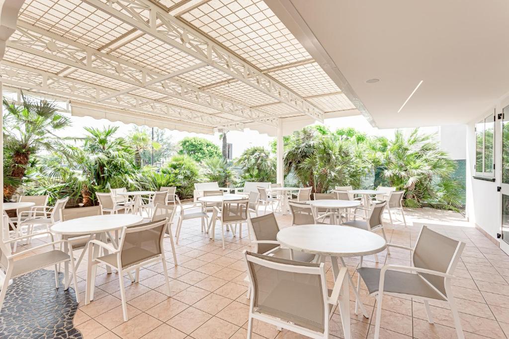 un patio extérieur avec tables, chaises et arbres dans l'établissement Hotel Blues, à Cervia