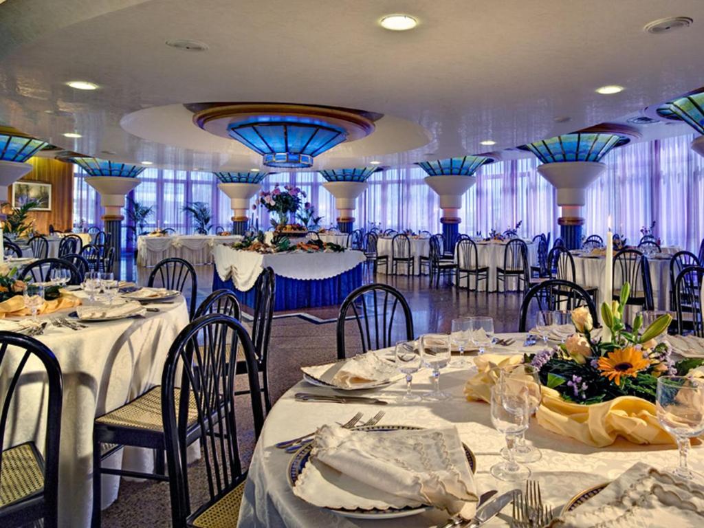 une salle de banquet avec des tables et des chaises blanches et des tons bleus dans l'établissement Hotel Le Tegnue, à Sottomarina