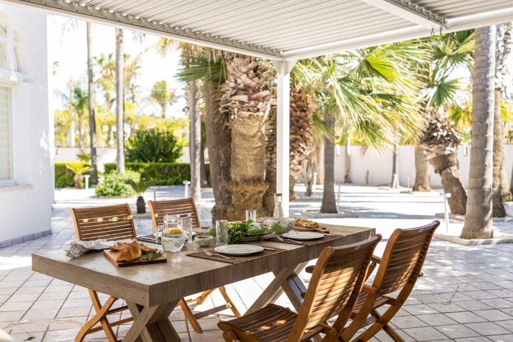 une table et des chaises en bois sur une terrasse avec des palmiers dans l'établissement Sea Relais Marsala, à Lido Signorino
