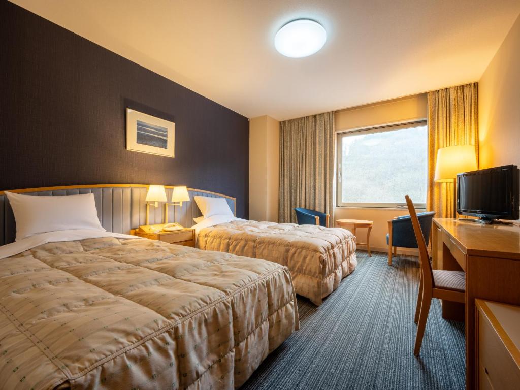une chambre d'hôtel avec deux lits, un bureau et une fenêtre dans l'établissement Hotel Kazuno, à Kazuno