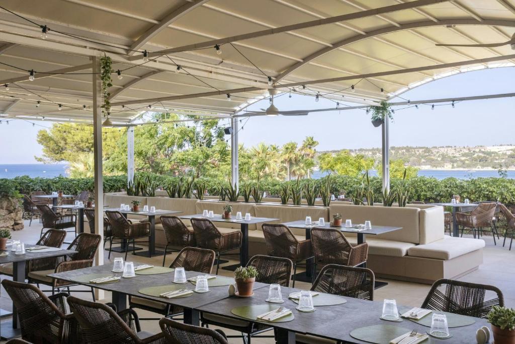 un restaurant avec des tables et des chaises et une vue sur l'océan dans l'établissement Mangia's Brucoli, Sicily, Autograph Collection, à Brucoli