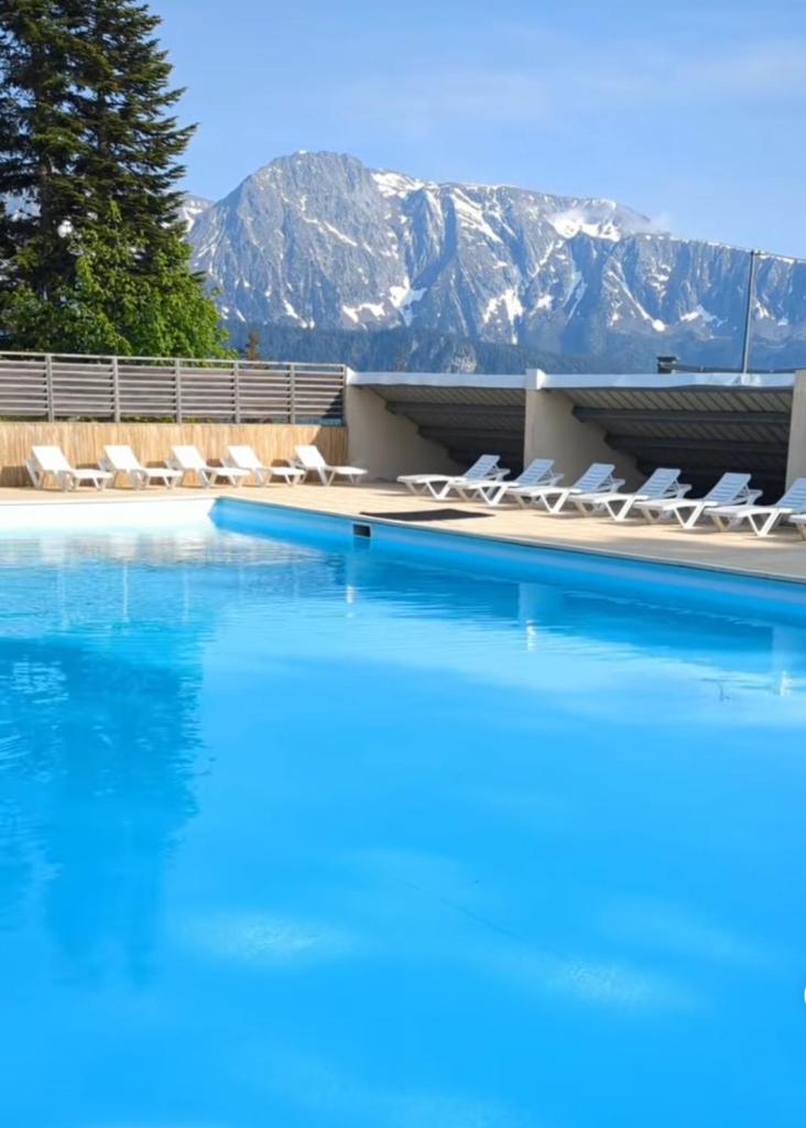 une piscine avec des chaises et des montagnes en arrière-plan dans l'établissement L'Après-ski Chamrousse 1700, à Chamrousse