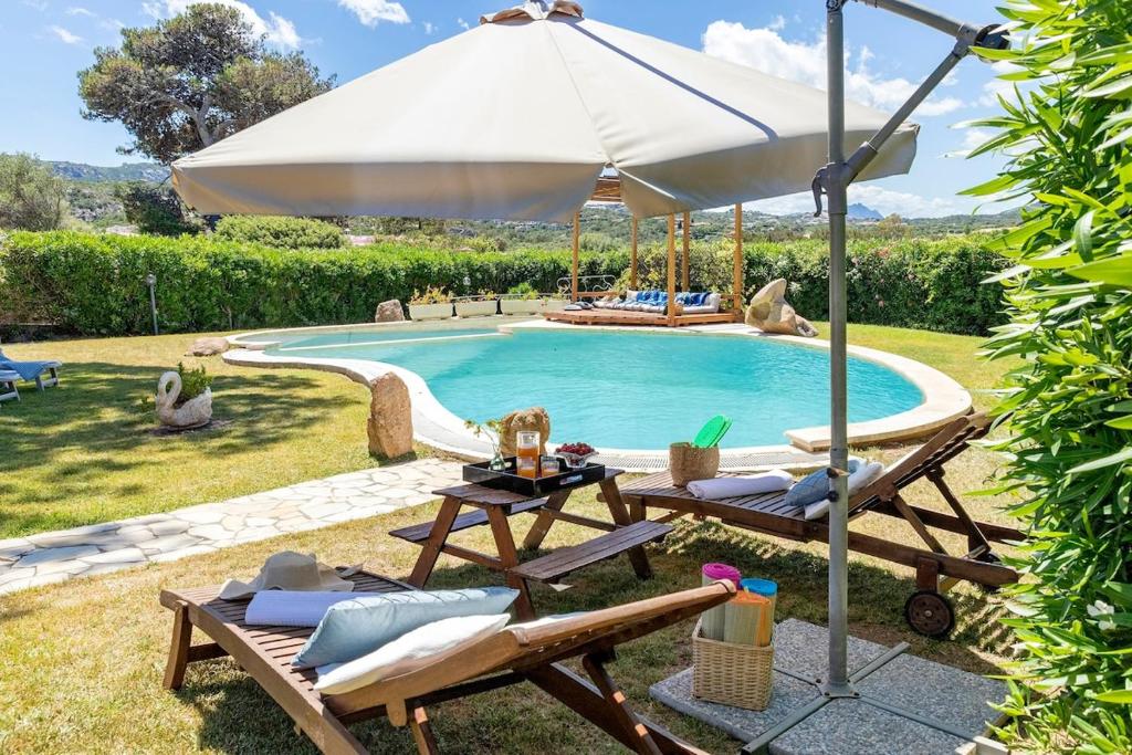 - une piscine avec un parasol, 2 chaises et une table dans l'établissement Villa con piscina e giardino, à Cala Bitta