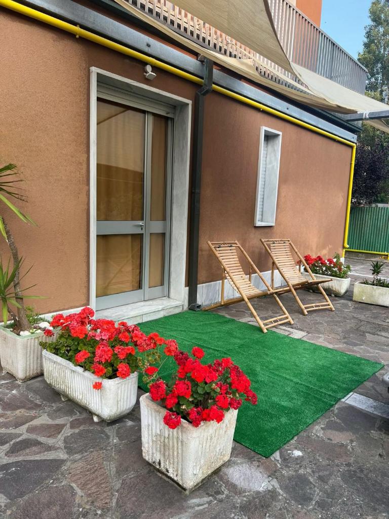 un patio avec des fleurs rouges et deux chaises et un sol vert dans l'établissement Hotel Nazionale, à Milano Marittima