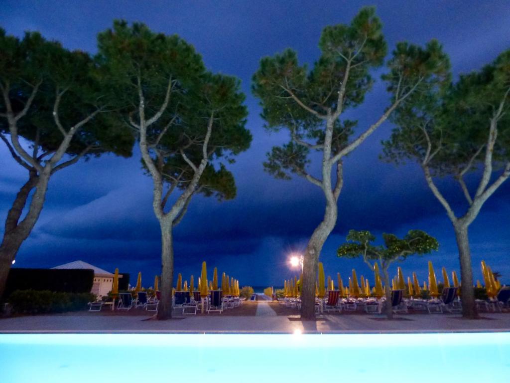 un groupe d'arbres avec des tables et des chaises la nuit dans l'établissement Mon Repos, à Lido di Jesolo