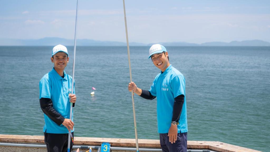 deux hommes en chemises bleues tenant des poteaux sur une jetée dans l'établissement Awakan, à Sumoto