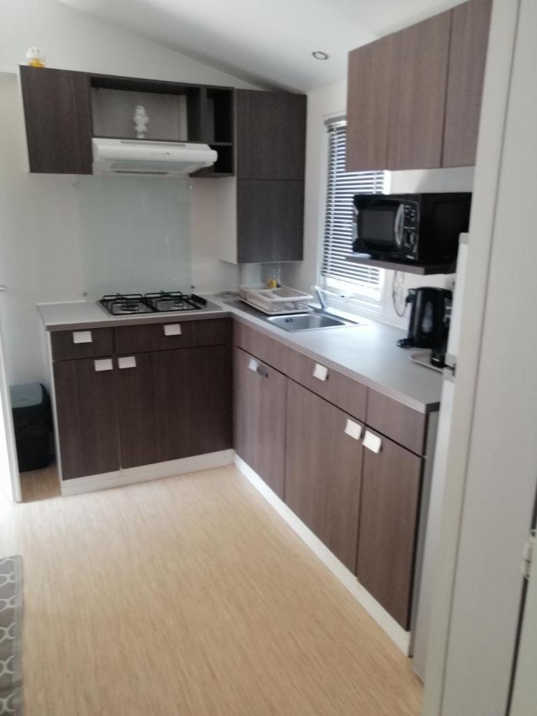 Elle comprend une petite cuisine avec des placards bruns et un four micro-ondes. dans l'établissement Mobil home Chez 118 Alain, à La Roque-dʼAnthéron 9 autres photos