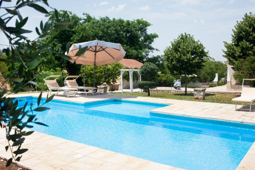- une piscine avec un parasol, deux chaises et une table dans l'établissement Trullo Alba, à Cisternino