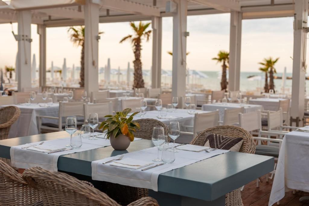un restaurant avec des tables et des chaises blanches et des palmiers dans l'établissement Excelsior Hotel, SPA & Lido - Preferred Hotels & Resorts, à Pesaro