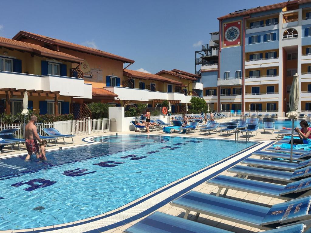 une grande piscine avec des chaises bleues et un hôtel dans l'établissement Villaggio Hemingway - Family Aparthotel, à Caorle