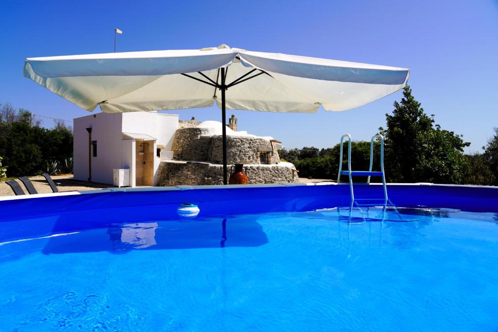 une grande piscine bleue avec un parasol dans l'établissement Trullo Il Ginepro - FASCINO MEDITERRANEO tra NATURA e STORIA, à Carovigno