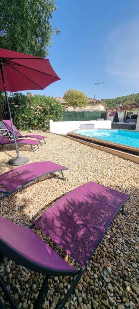 un groupe de chaises longues violettes et un parasol à côté d'une piscine dans l'établissement Le Gîte de la Fontaine - Aumes, à Aumes