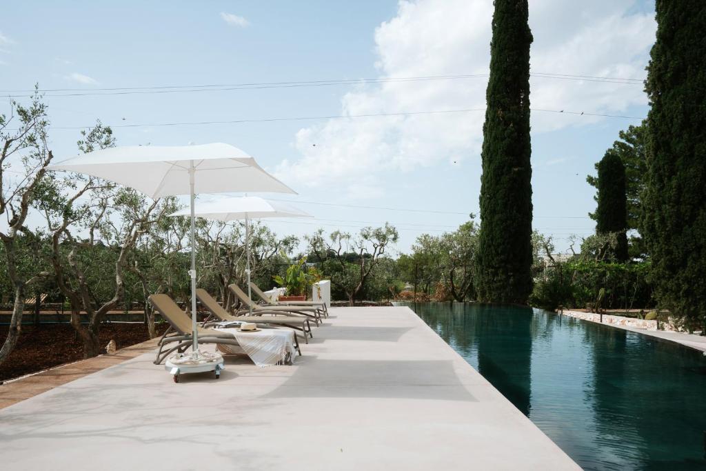 - une rangée de chaises longues et un parasol à côté de la piscine dans l'établissement Ostuni Escape Villa Galeone &infinity Pool 16x4m, à Ostuni