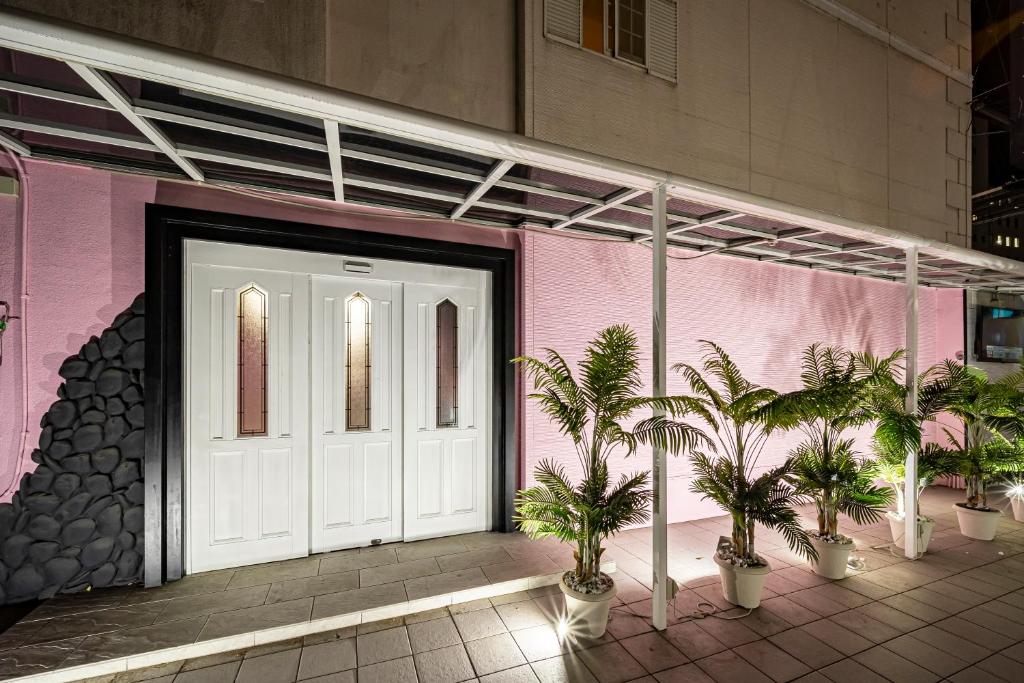 un bâtiment rose avec une porte blanche et des palmiers dans l'établissement Hotel Hu Namba (Adult Only), à Osaka